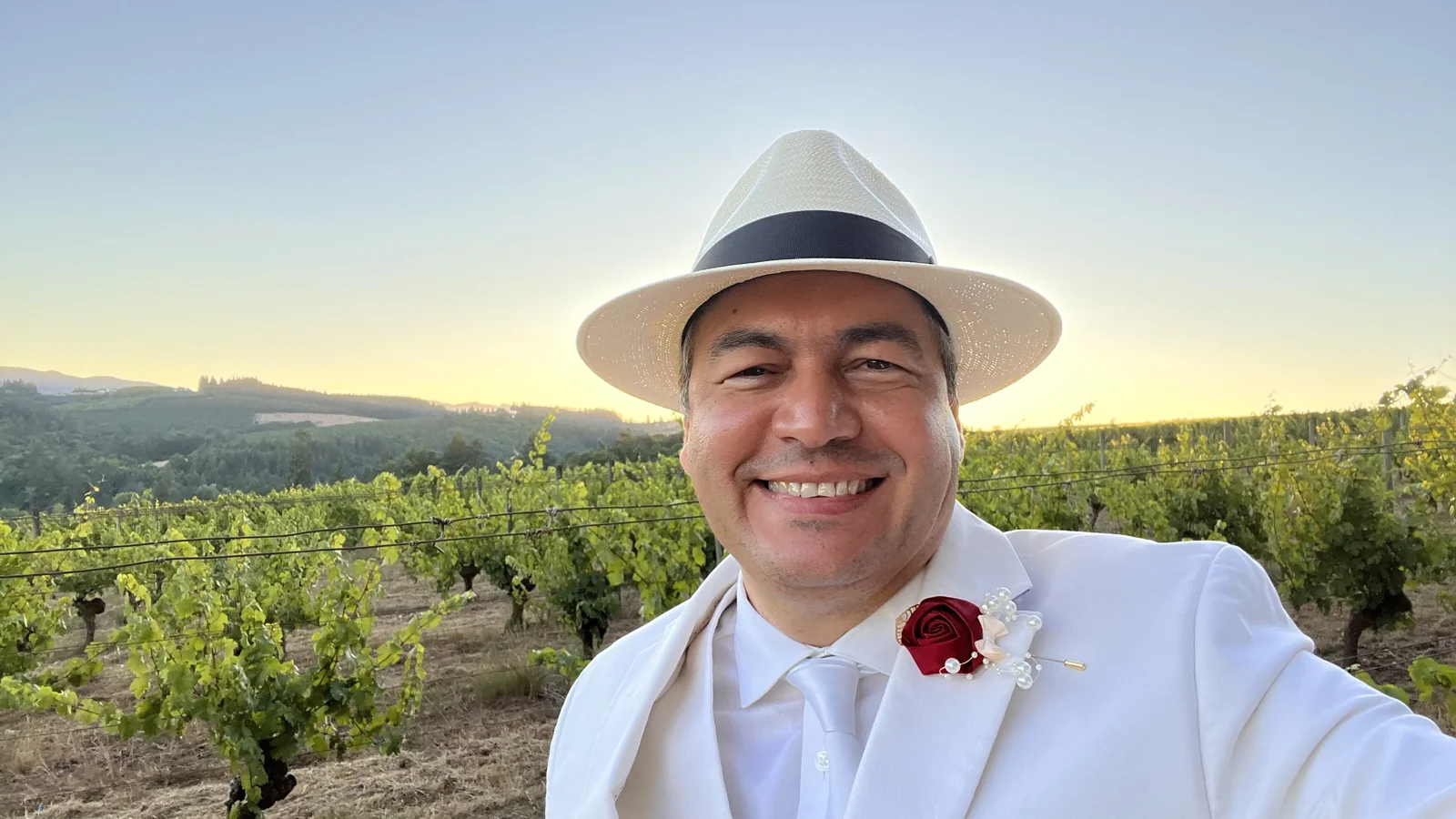 Author Tony Glez wearing a white suit and straw hat in a vineyard at sunset
